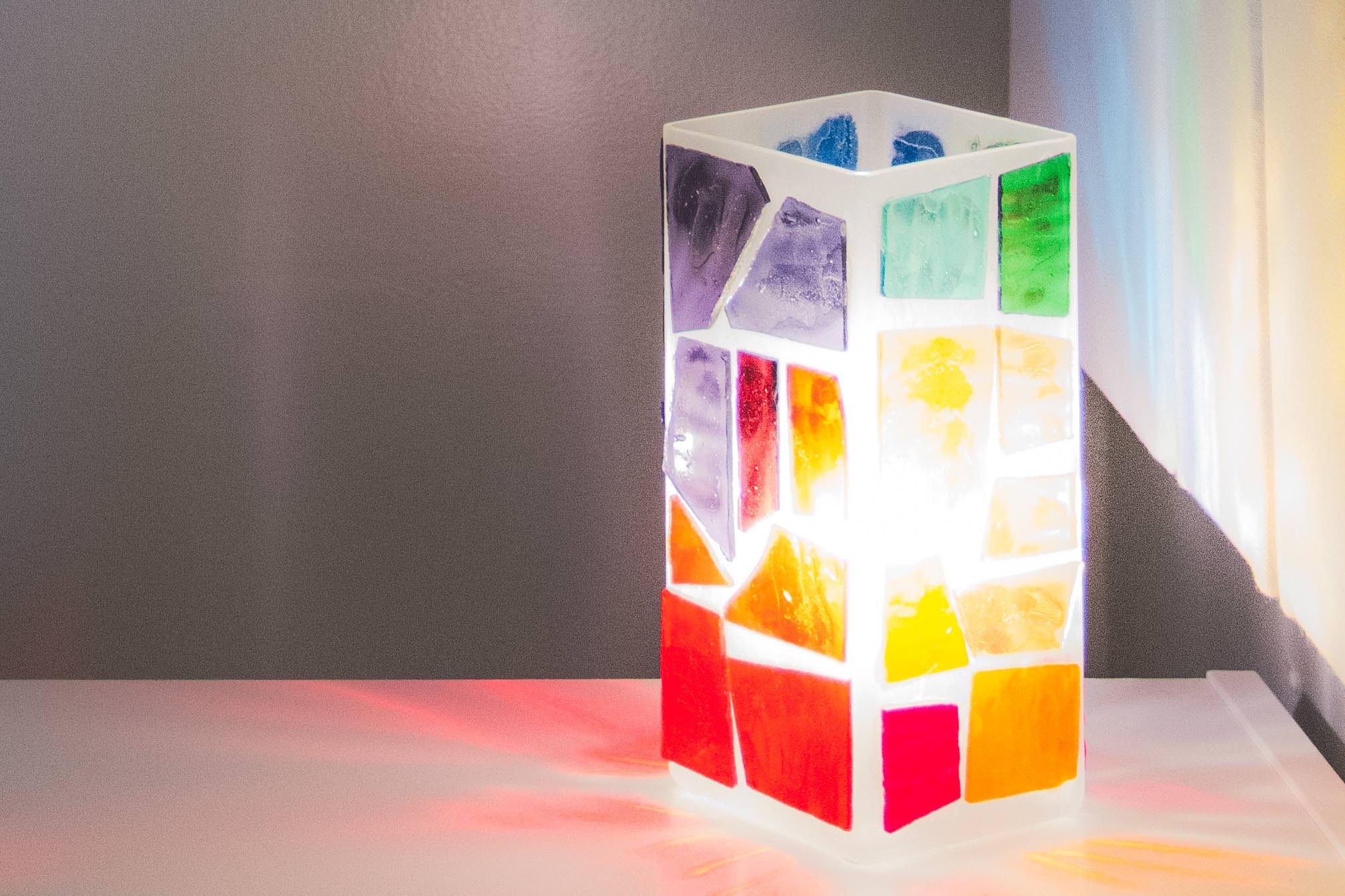 A colorful stained glass lamp with light shining through it.